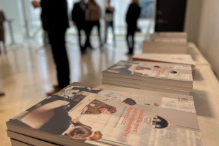 Stack of corporate annual reports on a table at a business event with attendees in the background.
