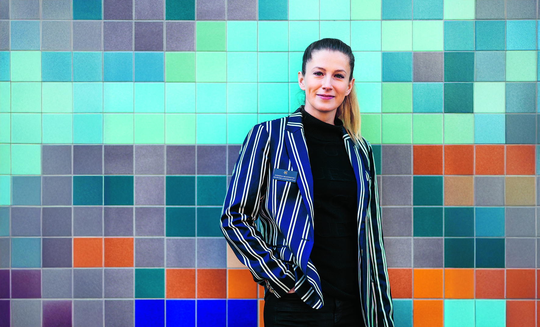 Woman in striped jacked leaned against colorful wall.