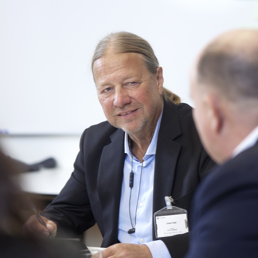 Professional man in business attire engaging in conversation at a conference with a name tag visible.
