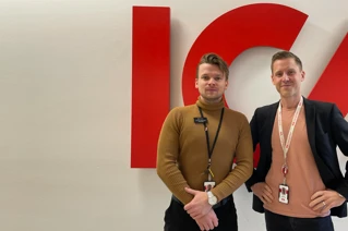 Two young men standing next to each other in front of a red logotype