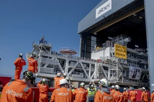Workers in orange overalls observing industrial equipment at an Aibel shipyard with Heidrun Equinor signage.