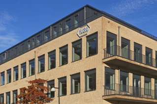 Modern corporate building exterior with brick facade, expansive windows, and company logo under a clear blue sky.