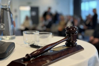 wooden gavel and sound block on a table, symbolizing authority and decision-making in a legal or formal setting, with a blurred background of seated people.
