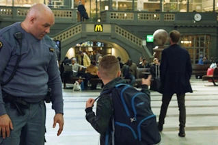 Security officer interacting with young boy in busy train station terminal.