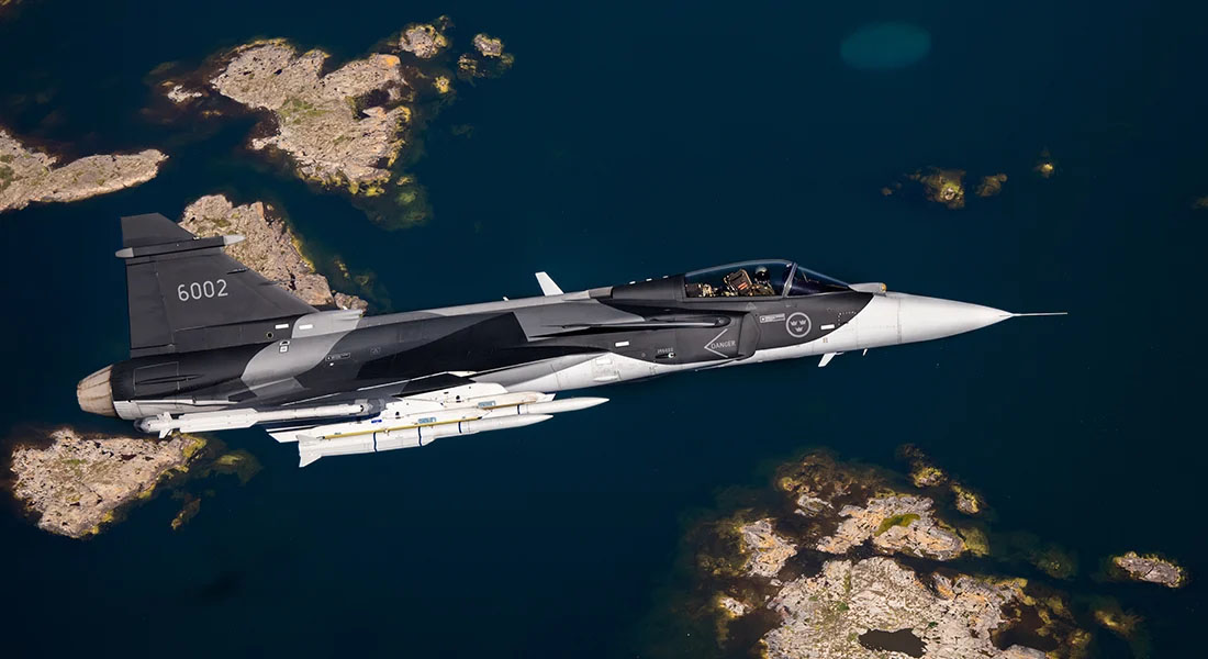 Military fighter jet flying over an archipelago with clear blue waters.