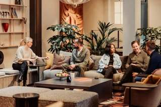 Modern office lounge area with a group of diverse professionals engaged in a casual meeting.