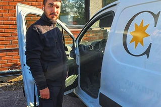 Man in work uniform standing next to a white van with a logo on the door.