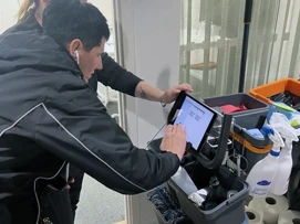 A woman standing next to a man tapping at a tablet on a Coor cleaning trolley.