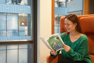 Woman sitting in orange chair reading a magazine