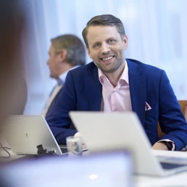 Portrait of man in a suit talking with coworkers at a conference-table.