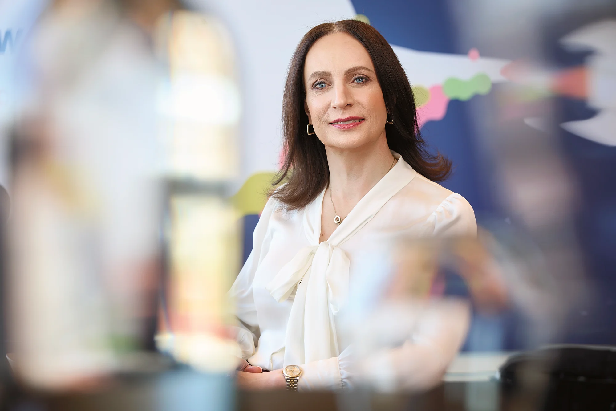 Caroline Farberger in a white blouse smiling in an office setting with blurred background.