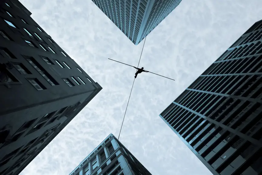 Man walking on a tightrope high up in the sky, surrounded by skyscrapers