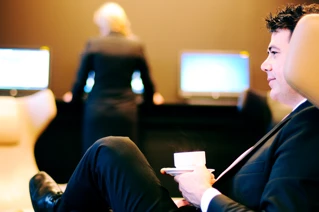 Businessman relaxing with coffee in modern lounge area with woman walking in the background