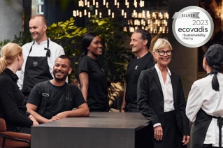 Medarbetare från olika serviceområden tar en paus tillsammans. Ecovadis silverbetygssymbol i det övre högra hörnet.