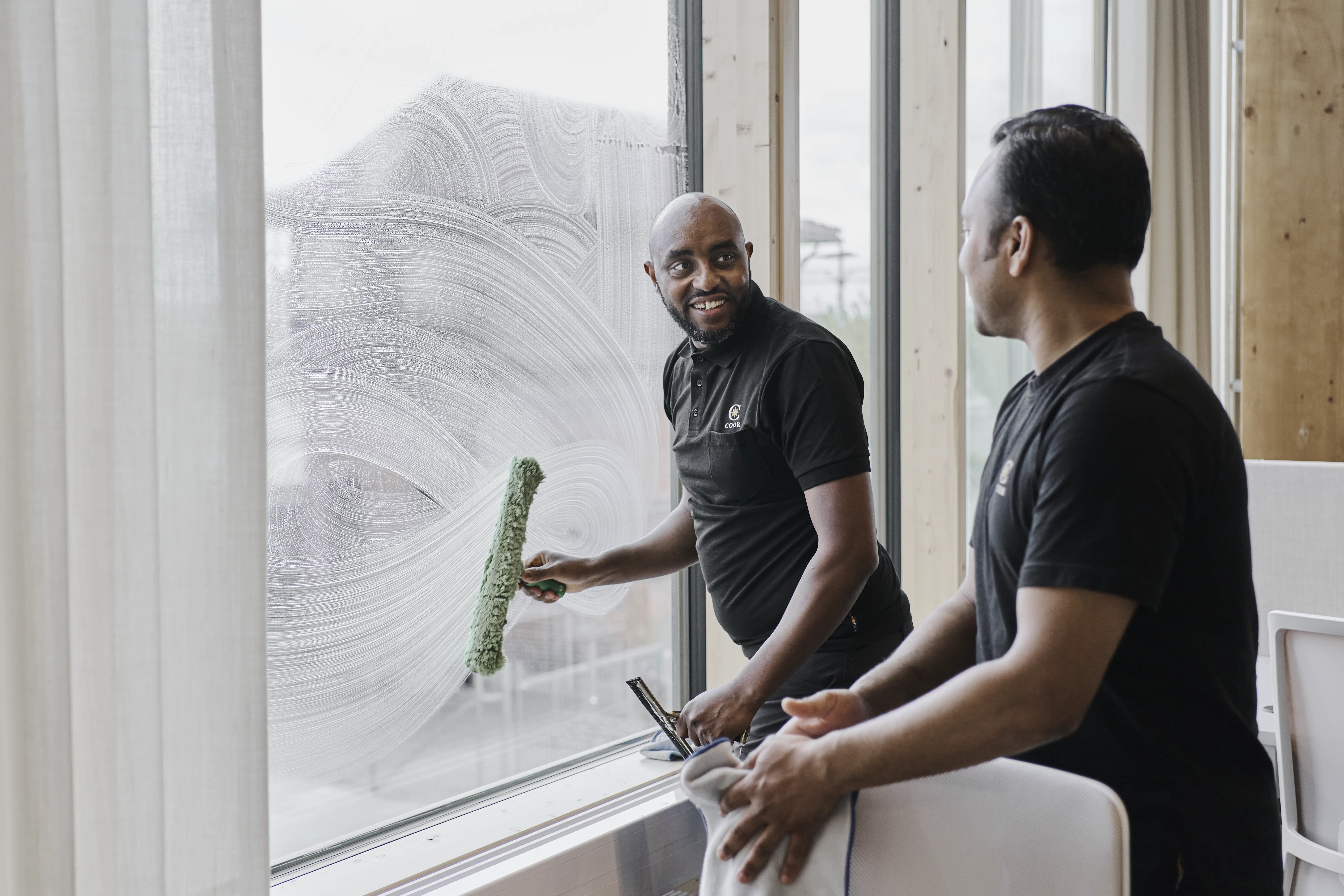 Two cleaners are cleaning an office window